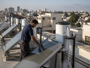 טכנאי מתקין מערכת מים סולארית על גג בניין משותף בישראל
